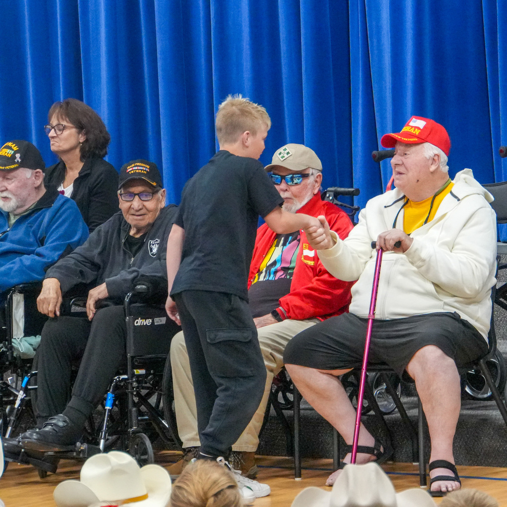 A student shakes hands with a few older veterans sitting in seats