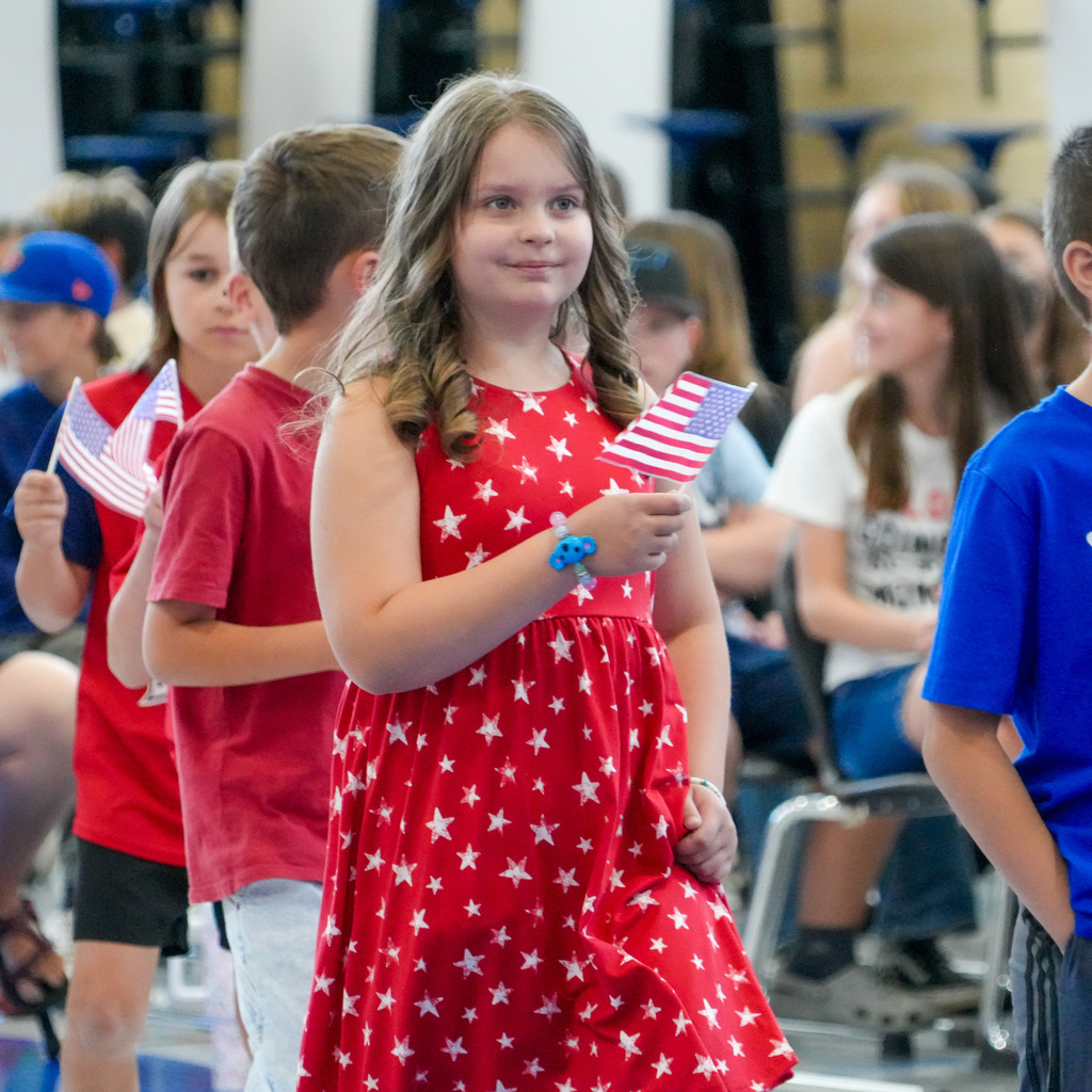 A young girl is walking with classmates holding a small American flag with a smile