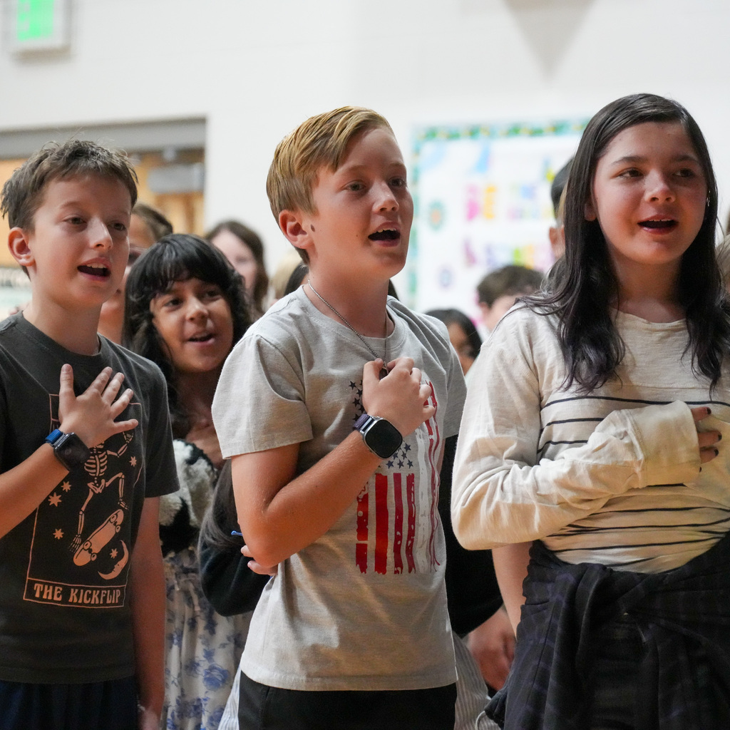 A few students stand with their hands over their hearts as they sing