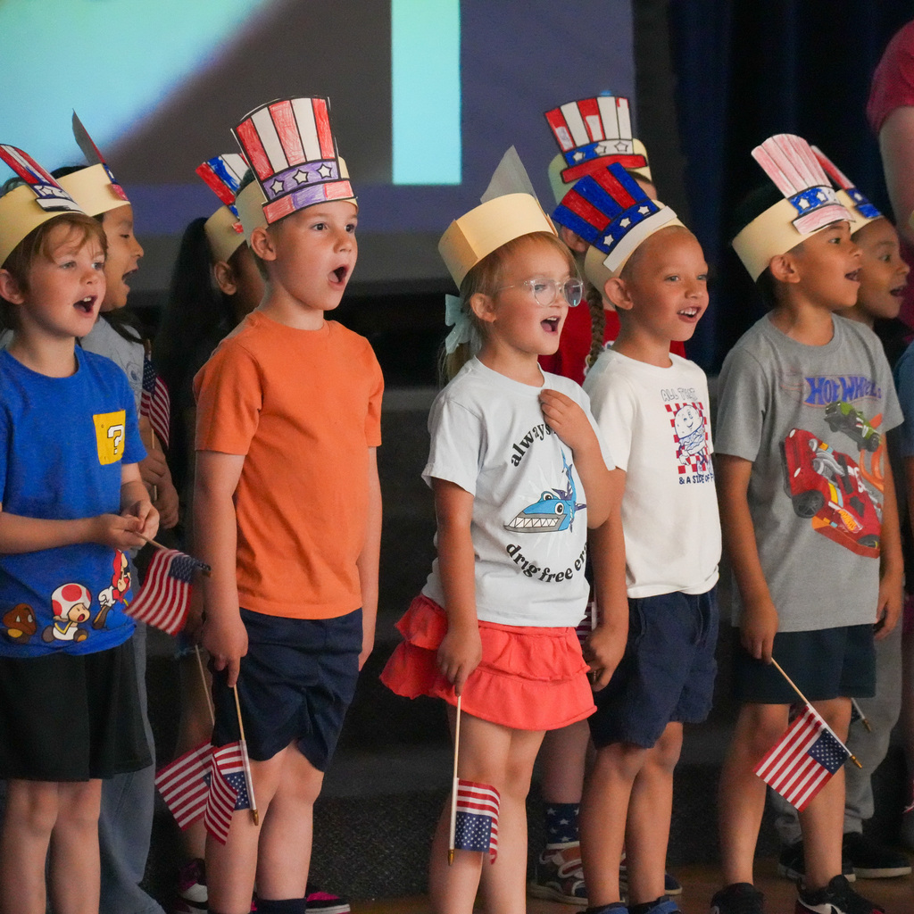 Younger students wearing American flag style top hats made of paper singing