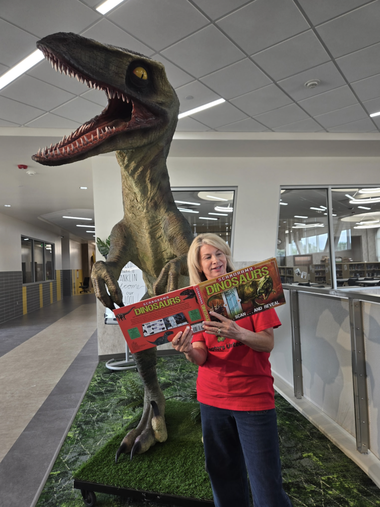 teacher reading a book in front of a large dinosaur
