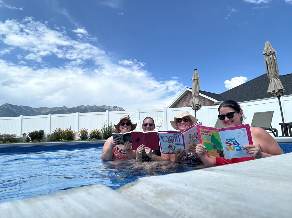 4 people sitting a a pool, reading books