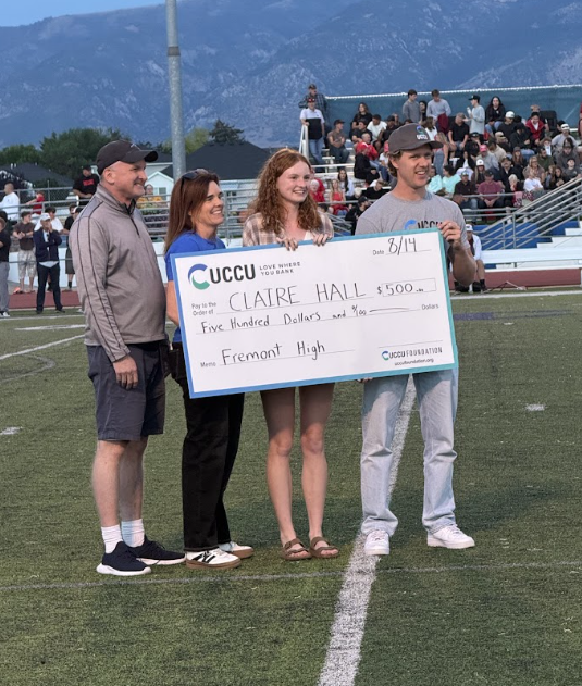 Claire Hall holds a check from UCCU with her family on the football field.