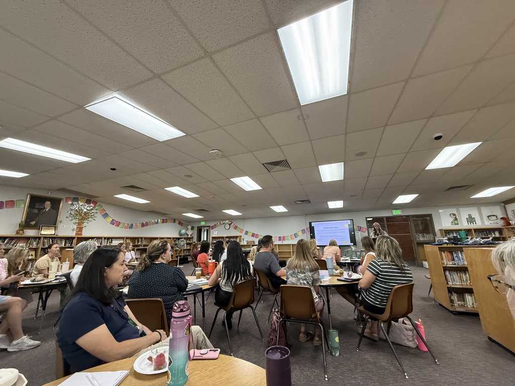 Teachers and staff seated at round tables in the Lomond View Elementary library during an intensive professional development session, focusing on a screen presentation at the front.