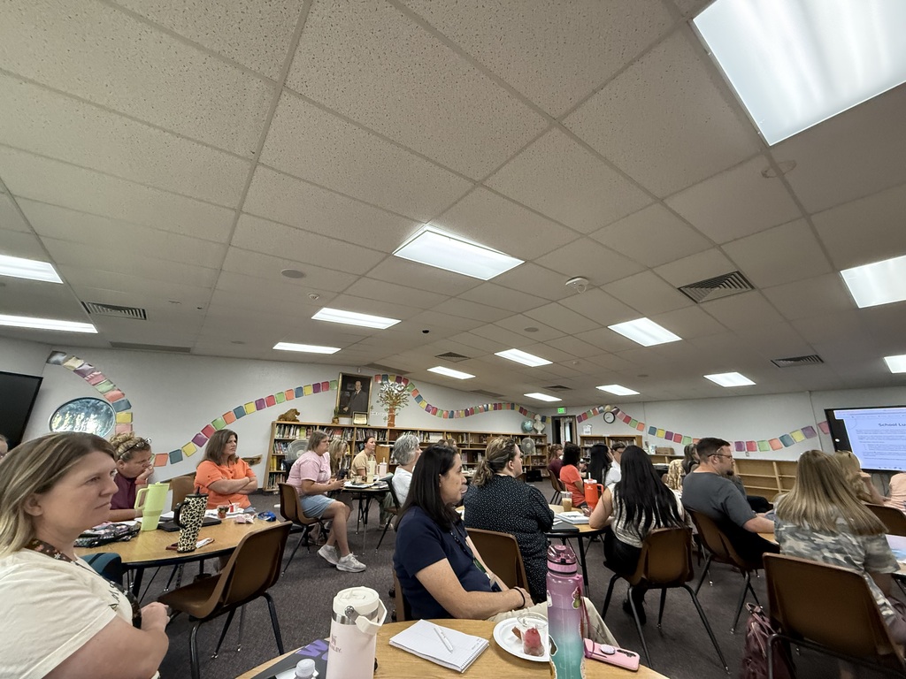 Teachers and staff seated at round tables in the Lomond View Elementary library during an intensive professional development session, focusing on a screen presentation at the front.