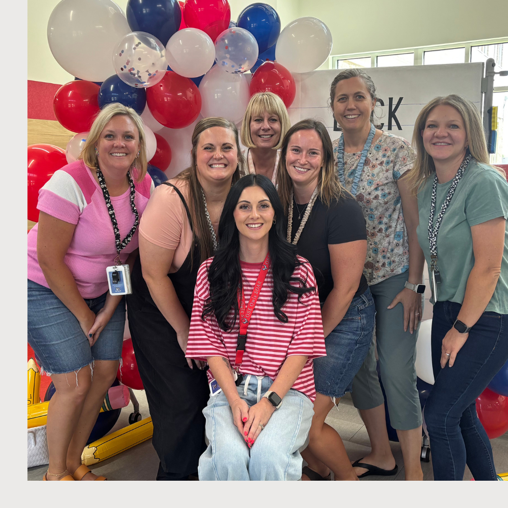 School aides in front of a Back to School Sign with balloon arch holding a OSE large pencil. Theme red, white, and blue.