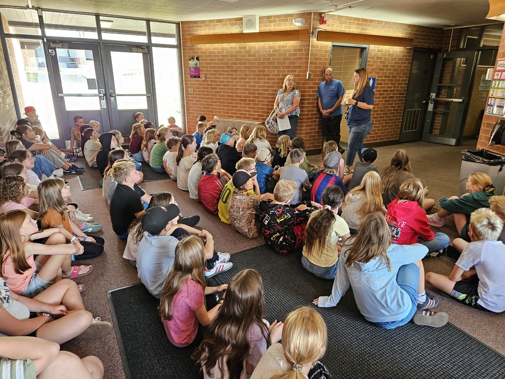 Students sitting on the floor near the entrance of the school restrooms as staff members go over bathroom expectations and safety.