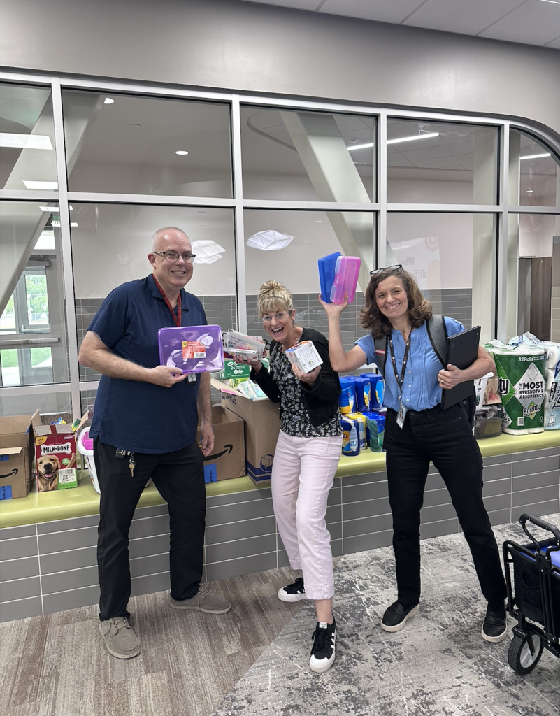 three smiling teachers posing and holding the donated supplies