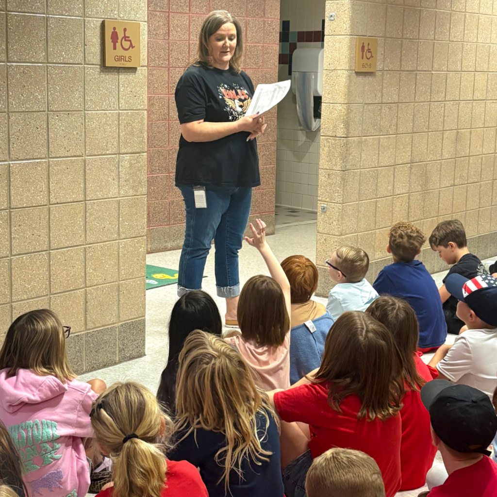 Students sitting on the floor listening to the rules and procedures of the school.