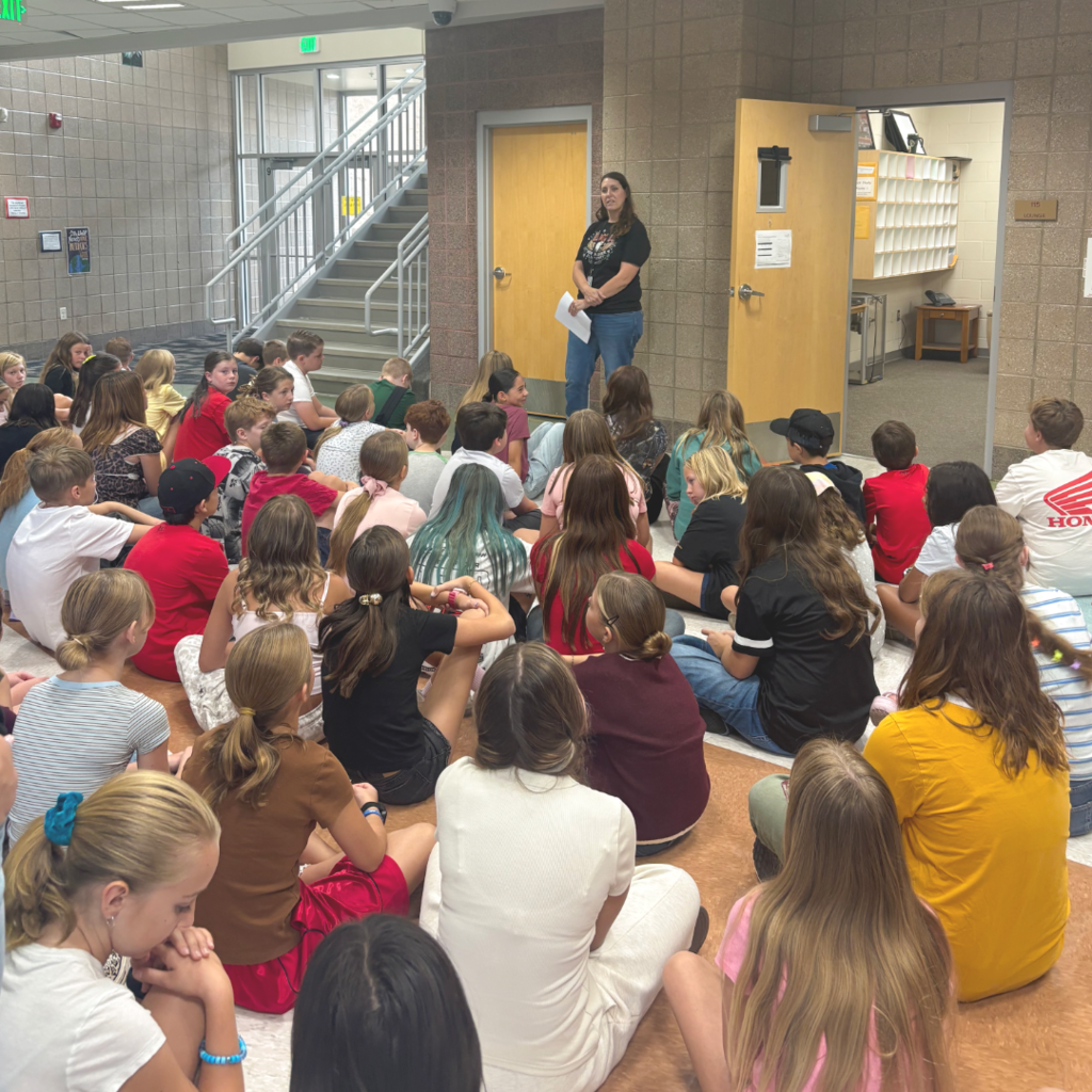 Students sitting on the floor listening to the rules and procedures of the school.