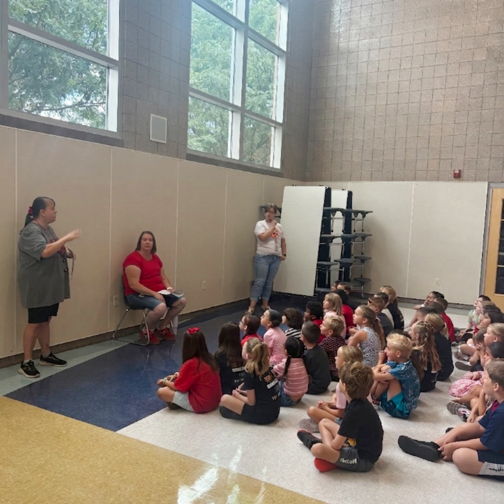 Students sitting on the floor listening to the rules and procedures of the school.