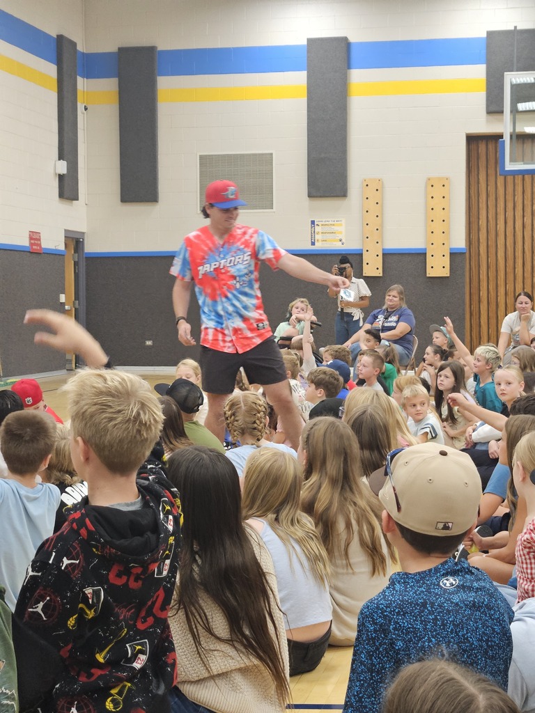 An Ogden Raptors baseball player walking through a crowded gym floor as students raise their hands to interact with him.