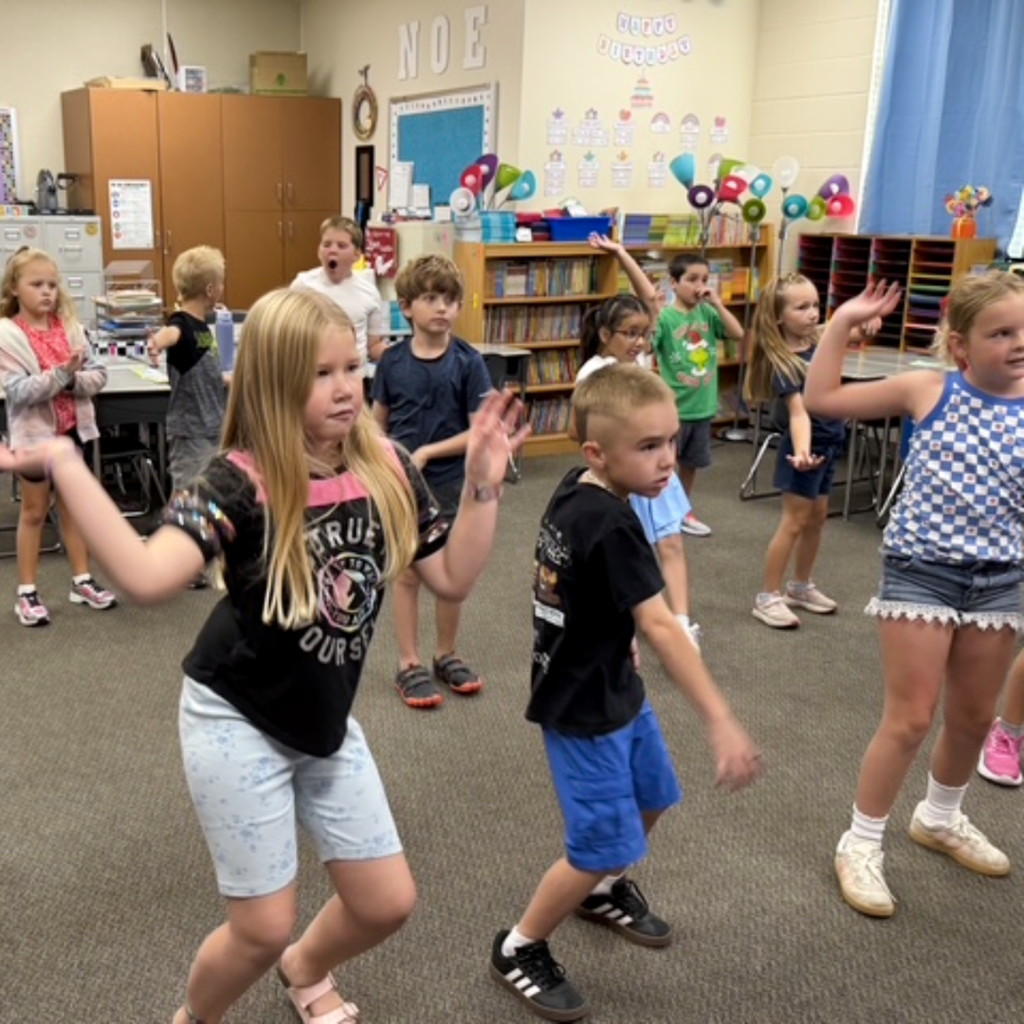 A class of students standing in their classroom moving to the music.