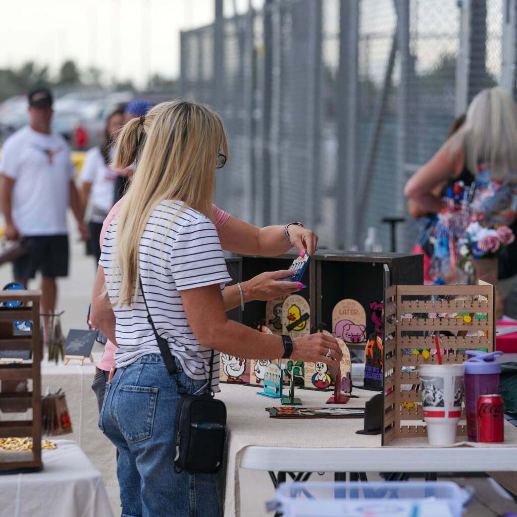 A woman browsing handmade craft displays at an outdoor school community event booth.