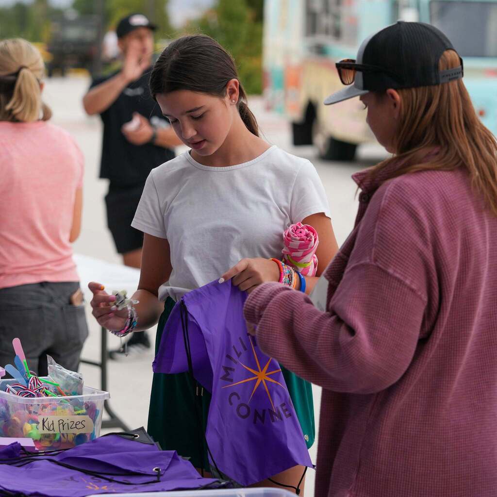 A young student looking into a purple prize bag at an outdoor school event table.