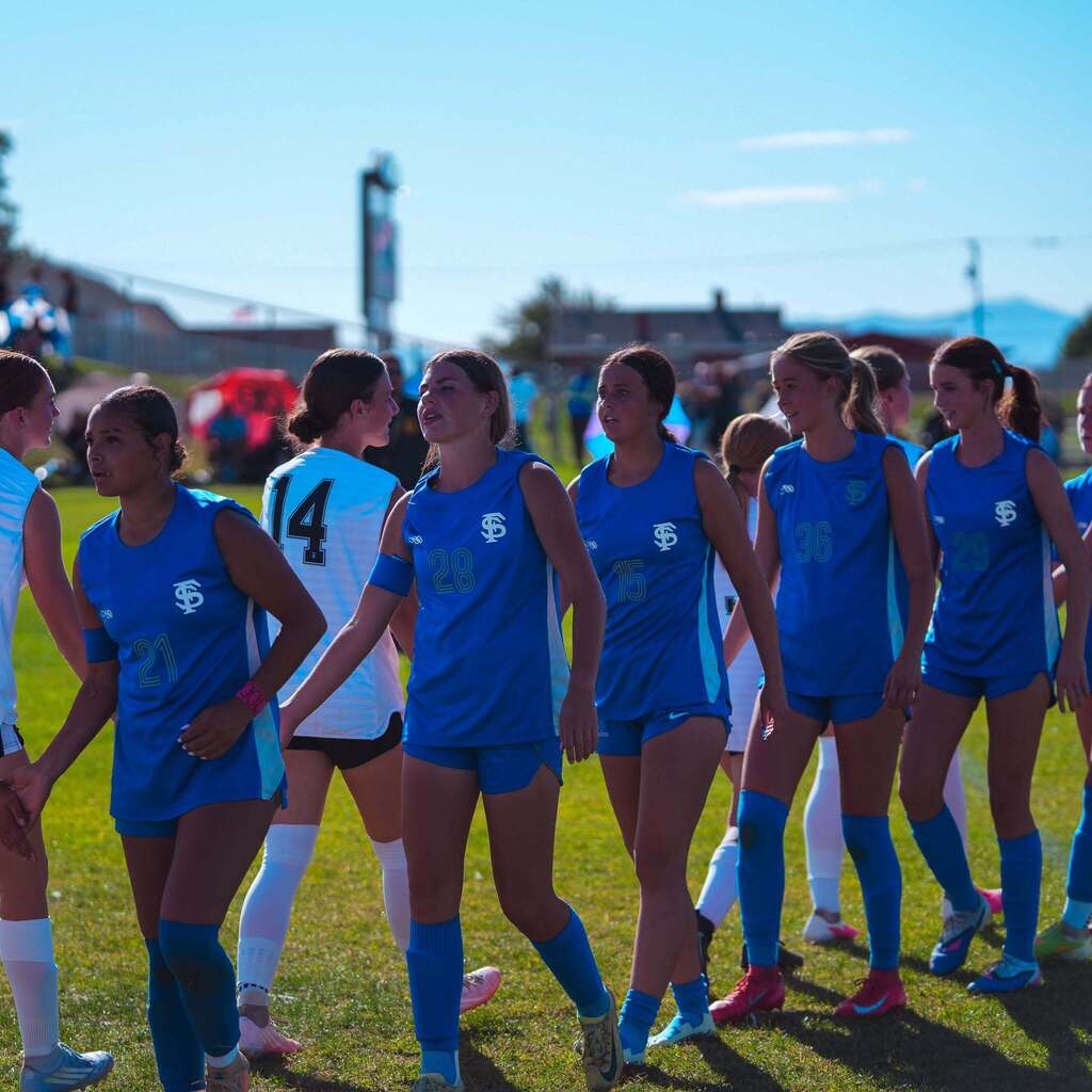 Players from both high school soccer teams walk side-by-side on the field, shaking hands and displaying good sportsmanship after the match.
