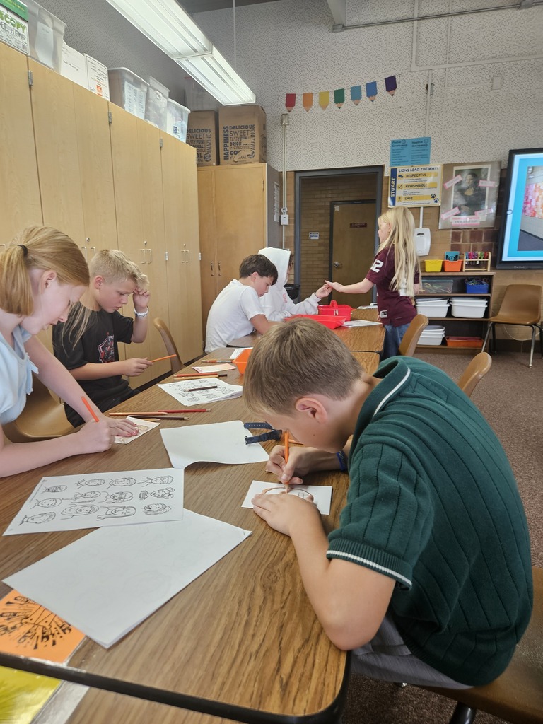Students seated at classroom tables working intently on small self-portrait art sketches using colored pencils.