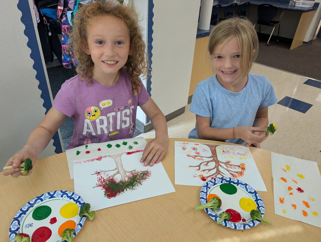 third grade students smiling and making paintings with broccoli instead of paint brushes