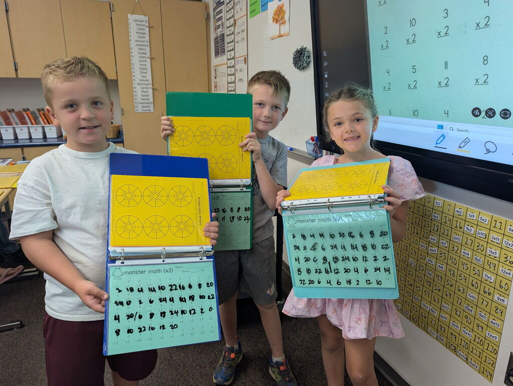 Students holding up work books and smiling, working on math facts