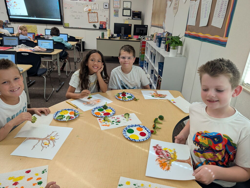 third grade students smiling and making paintings with broccoli instead of paint brushes
