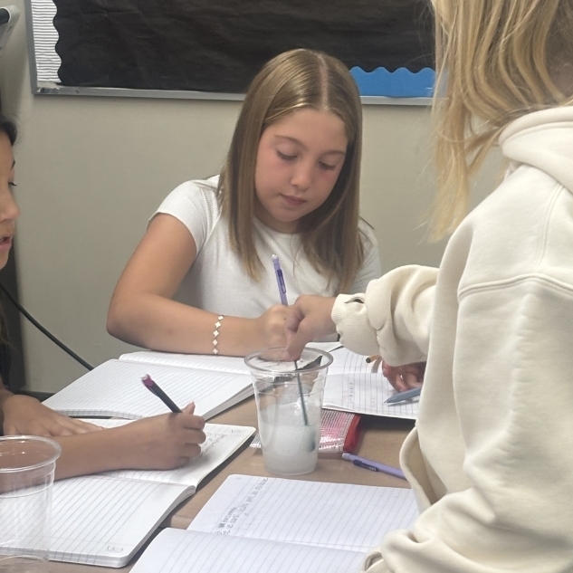 girls writing and doing a science experiment