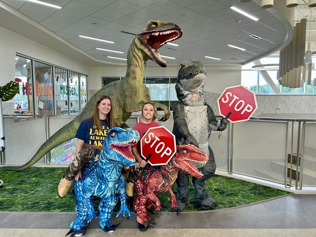 three crossing guards standing in front of a rator statue holding a stop sign dressed as raptors.