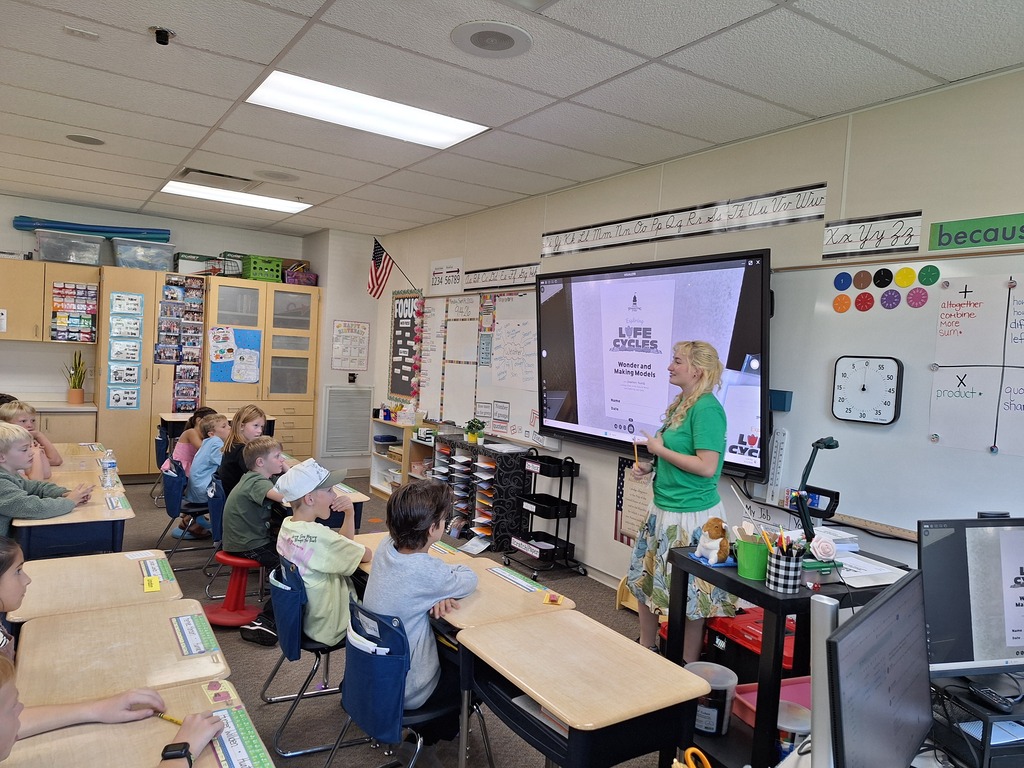 A teacher presenting a lesson titled "Life Cycles" to elementary students in a classroom.