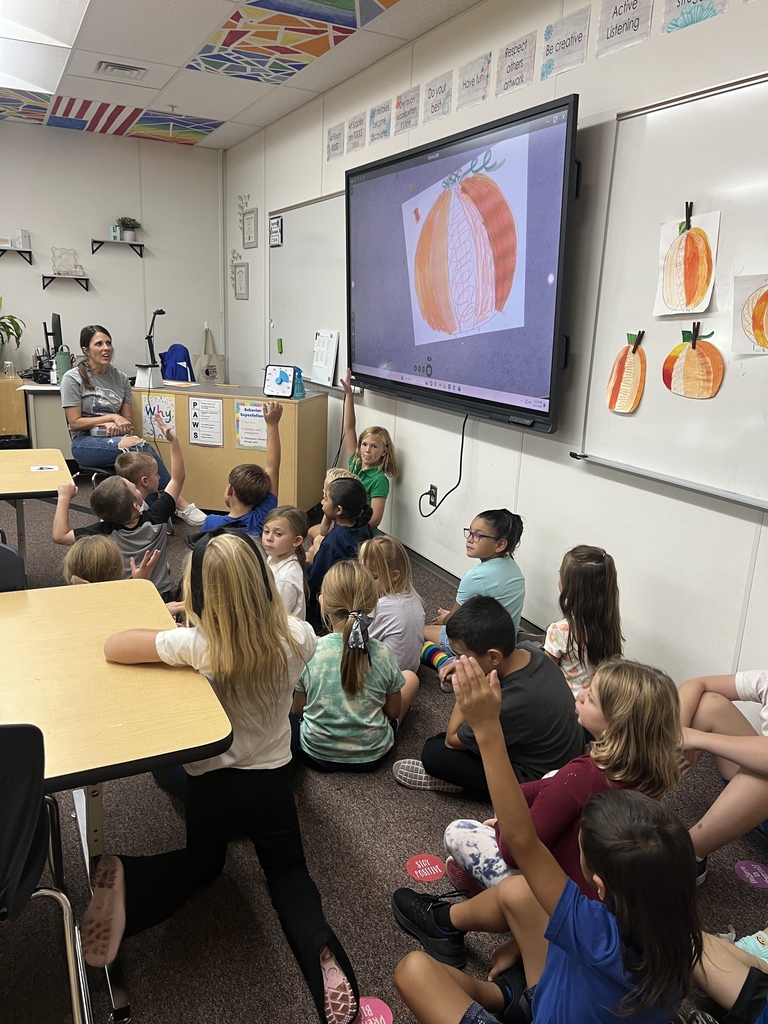 Mrs. Hibbert the art teacher showing a pumpkin on a screen and second grade students are sitting and listening to her