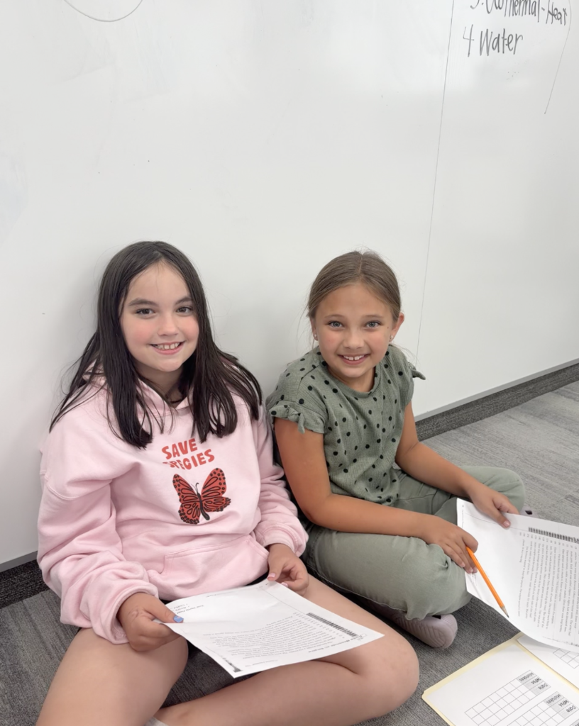 2 girls sitting and holding paper while smiling