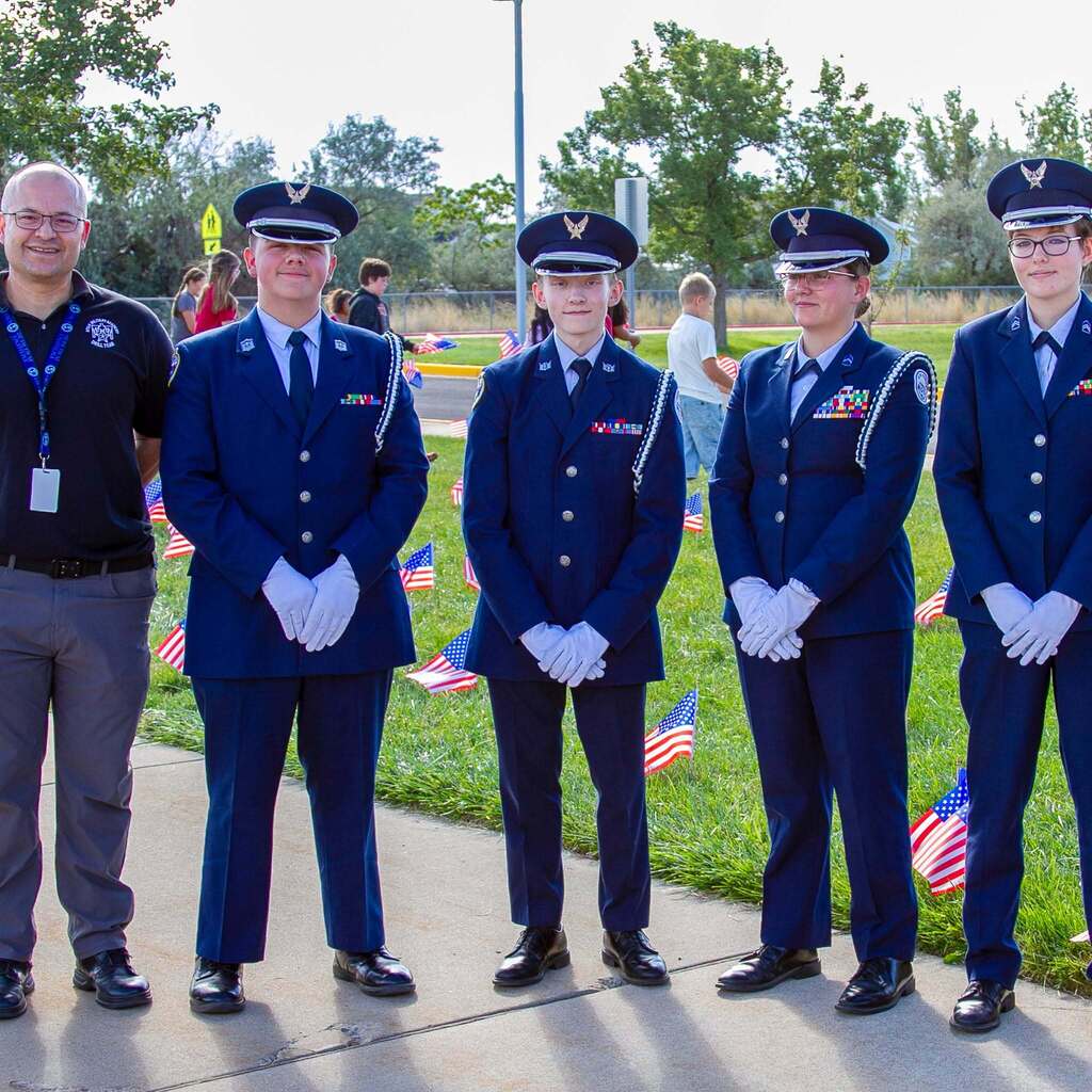 Four youth members of the Utah Military Academy Honor Guard in full dress uniforms stand at attention alongside an adult leader on the sidewalk in front of West Haven Elementary.