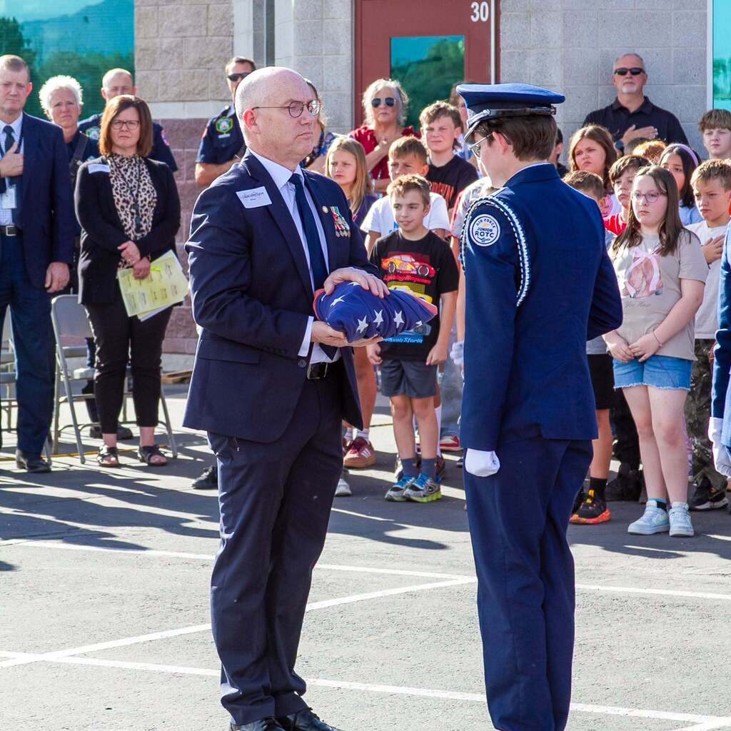A distinguished guest in a suit holds a ceremonially folded American flag while standing face-to-face with an Honor Guard member during the flag retirement proceedings.