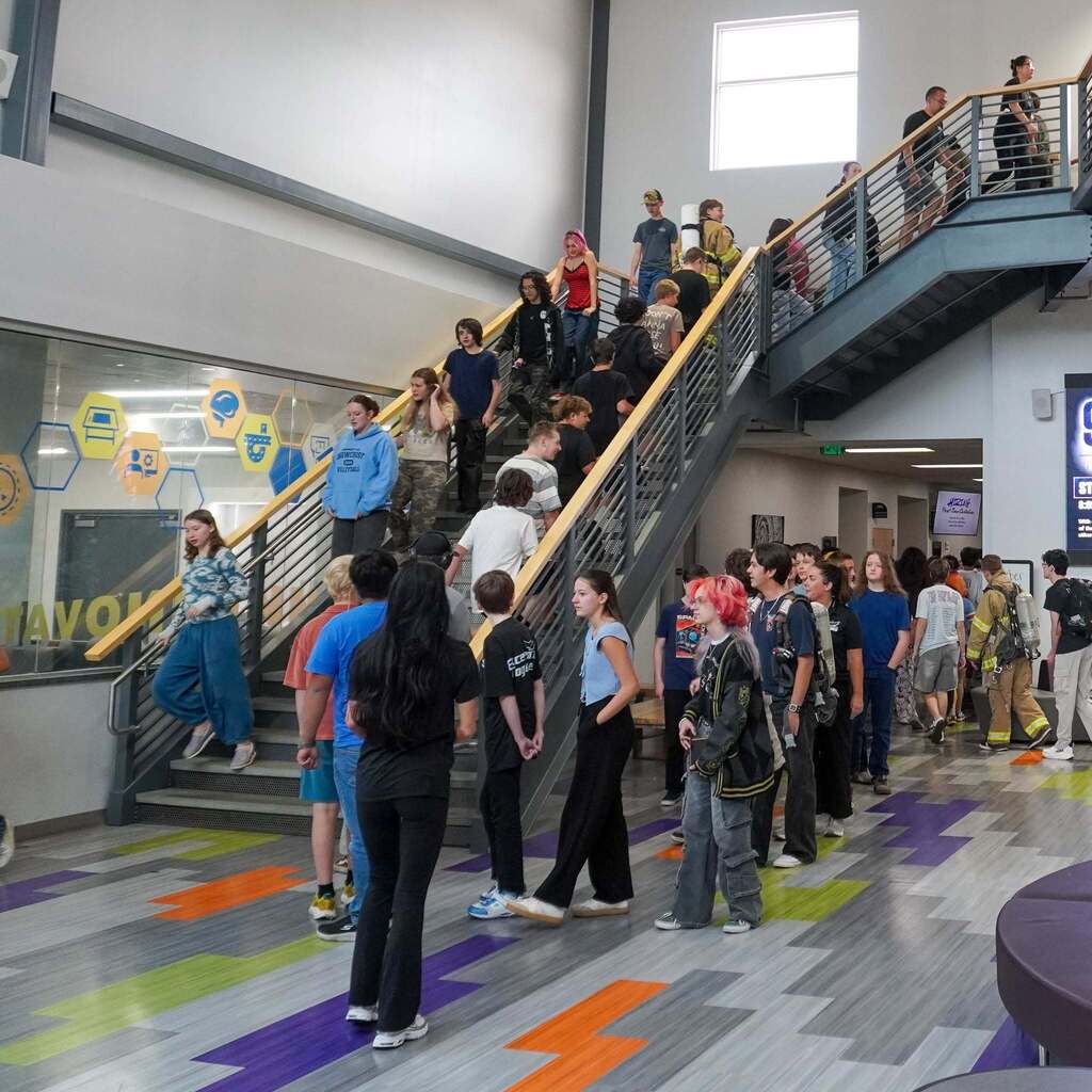 High school students at Innovation High walk down an open interior staircase in a multi-story atrium during a 9/11 remembrance stair climb event.