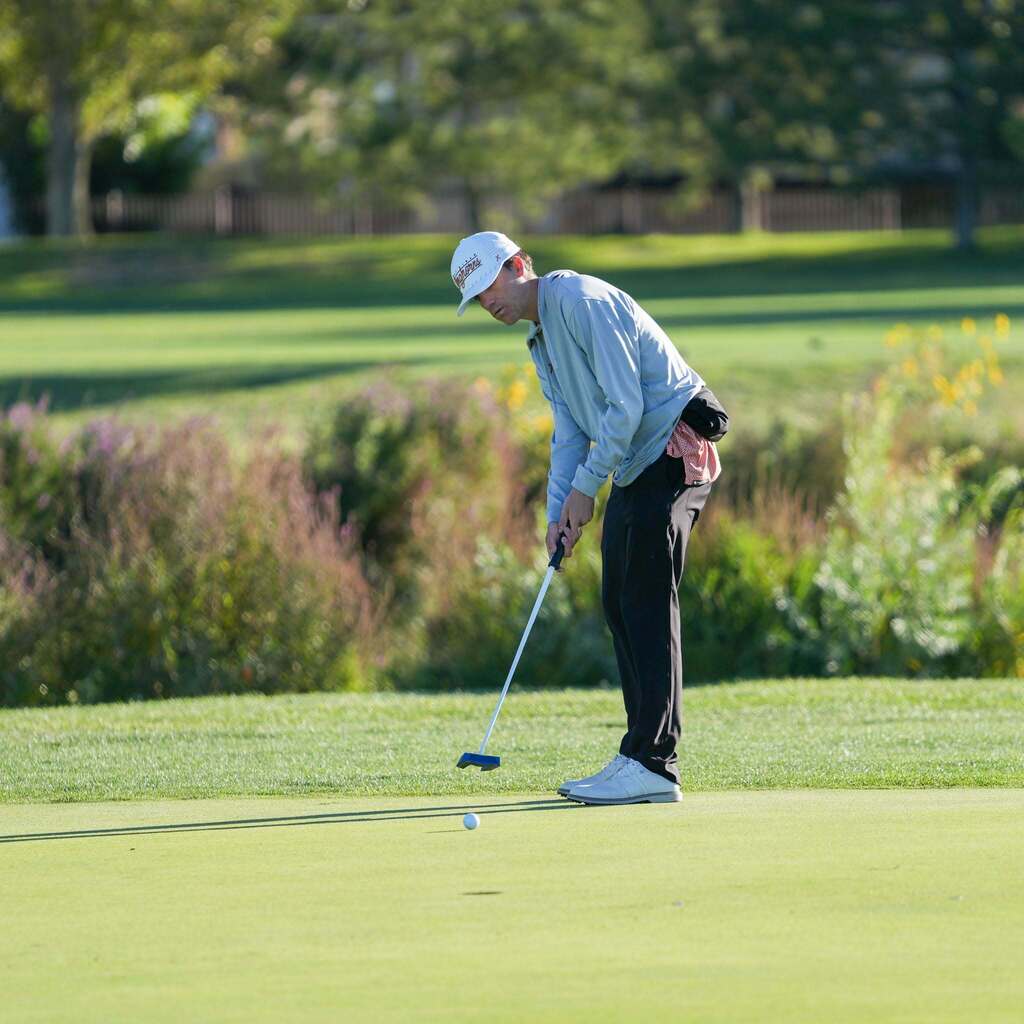 A golfer wearing a Longhorns visor stands over a putt on a lush green, lining up his stroke toward the cup.