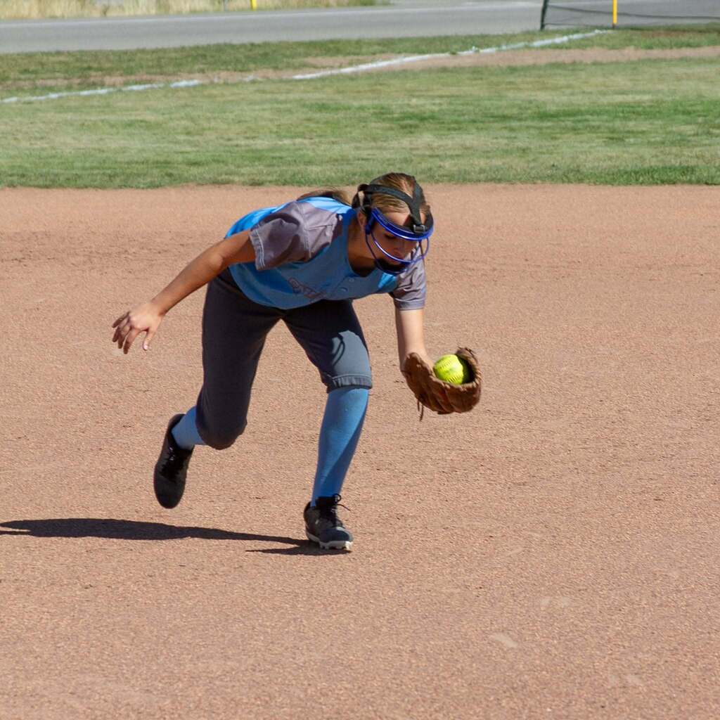 A Snowcrest player bends down to field a sharp ground ball cleanly on the dirt during the game.