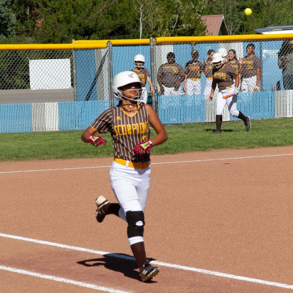 A Sand Ridge Junior High softball player wearing a brown pinstripe Scorpions uniform and batting helmet rounded the bases and sprints toward home plate.