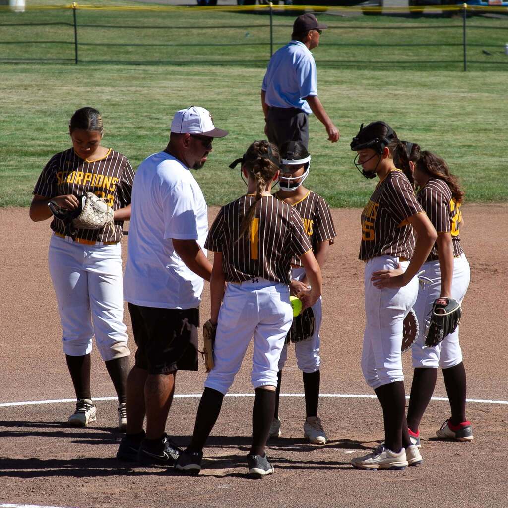 A Sand Ridge Junior High softball coach gathers his team in the pitcher's circle for a mound conference during the game.