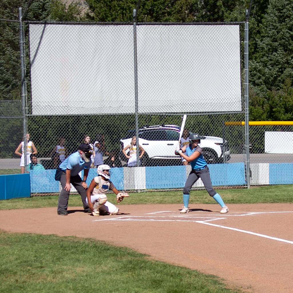 A Snowcrest batter takes her stance at the plate with the umpire and catcher positioned behind home plate.