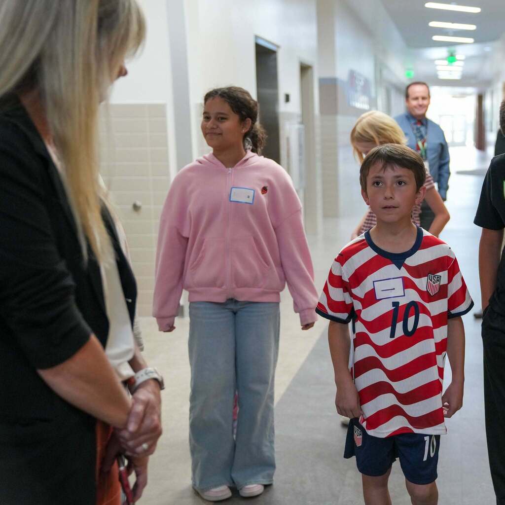 Two Roosevelt Elementary student ambassadors speak with Representative Katy Hall in the school hallway.