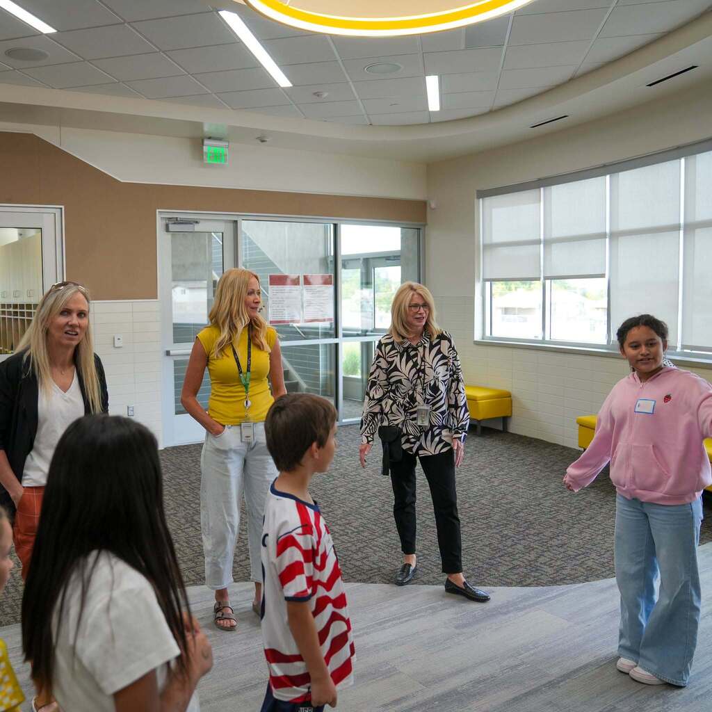 Representative Katy Hall and Roosevelt Elementary school administrators listen as a student ambassador gesturally presents in a open learning area.