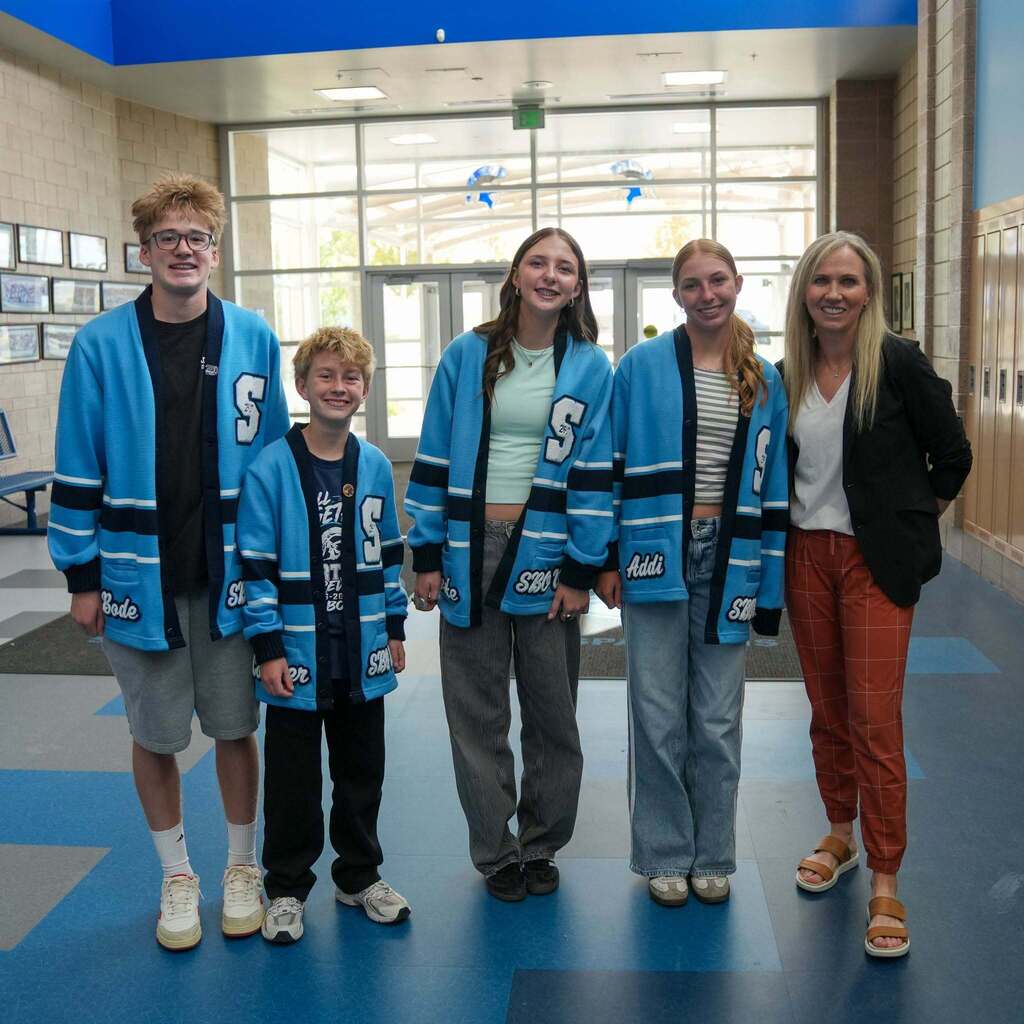 Representative Katy Hall stands in a school hallway with four South Ogden Junior High Student Body Officers wearing matching blue and white SBO cardigans.