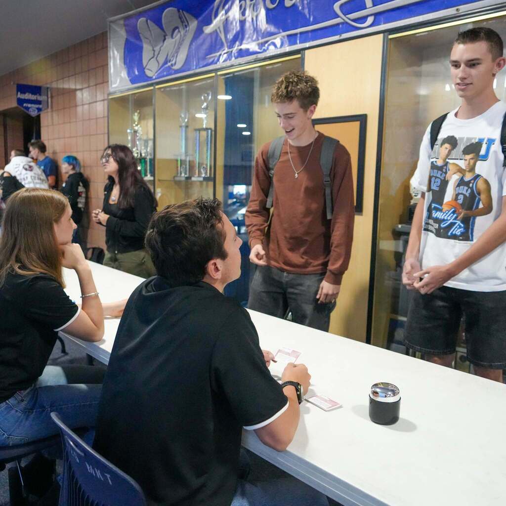 Two male students present their pitch across a table to judges, standing under a sign that reads "Fremont High School Performing Arts" in the school concourse.