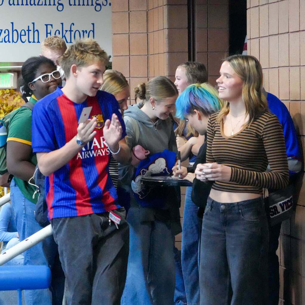 A group of Fremont High School students gathered around a table in the hallway, smiling and chatting enthusiastically during the DECA Wolf Tank competition.