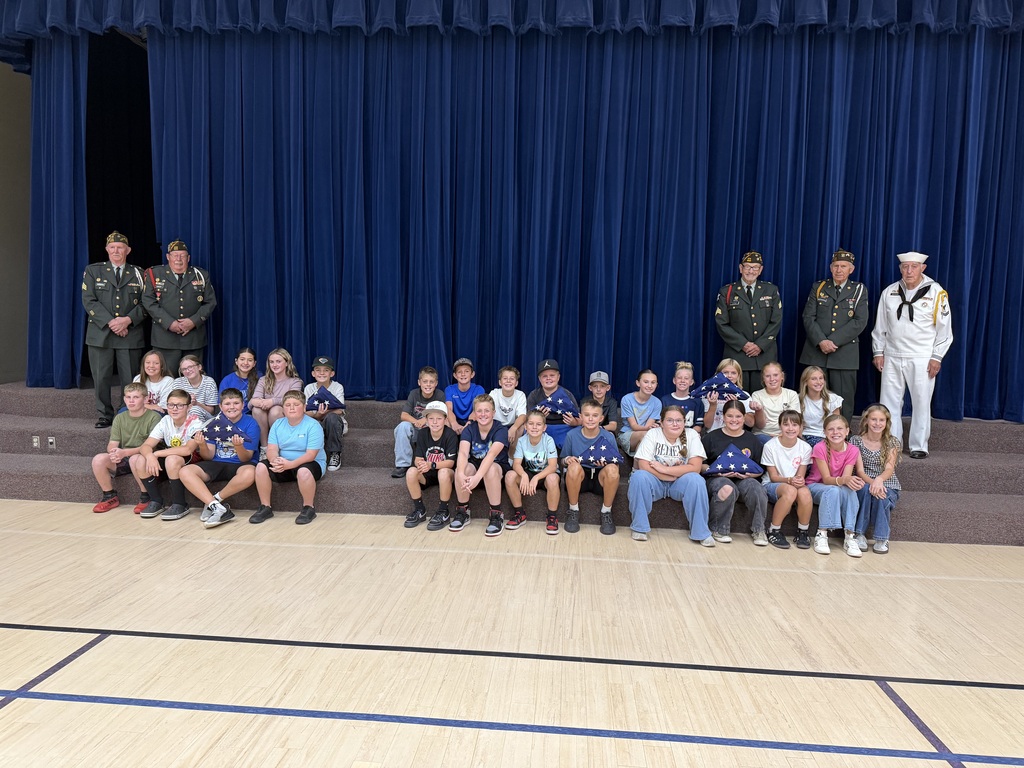 class of 6th grade students smiling with the veteran volunteers and their folded flags