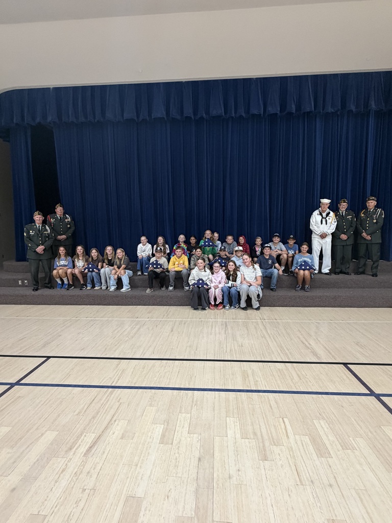 class of 6th grade students smiling with the veteran volunteers and their folded flags