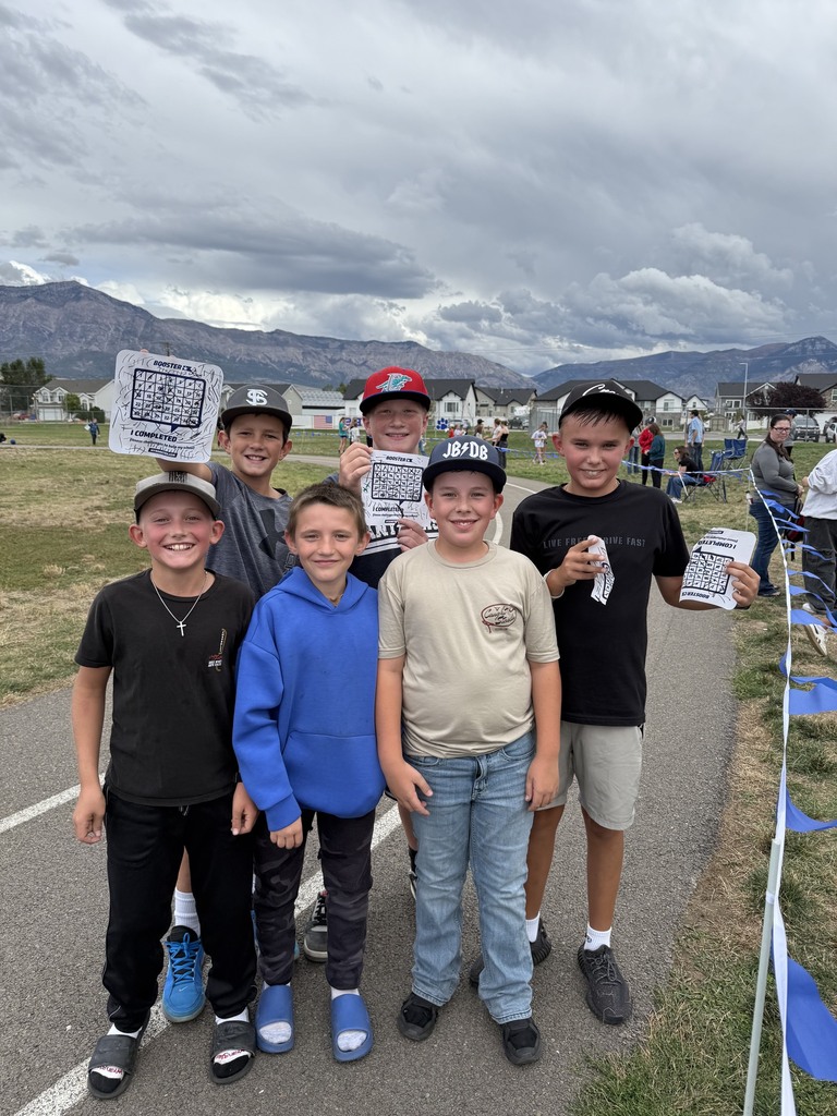 group of male students holding up their lap sheets and smiling in front of the track and mountains in the background