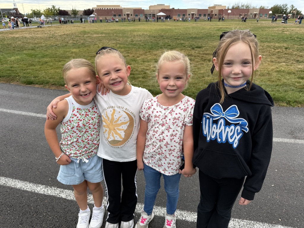 group of female students smiling on the track with the school in the background