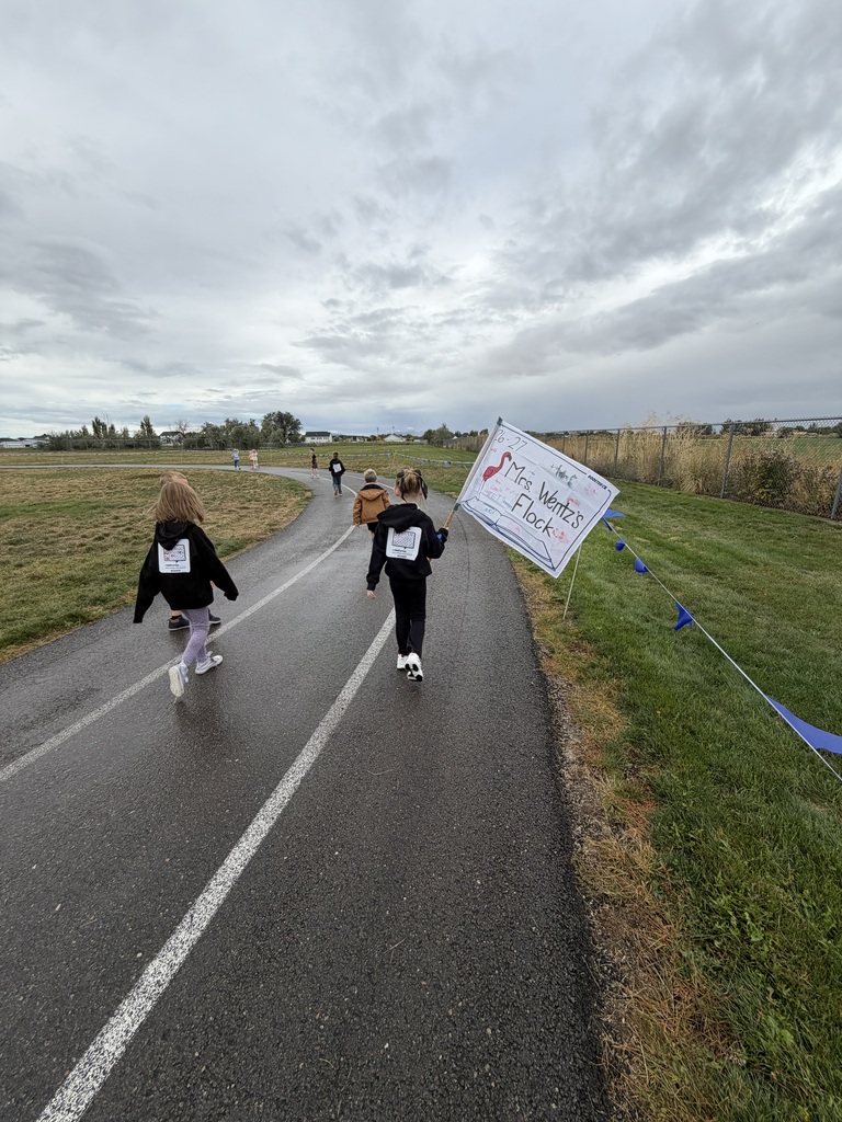 students running on the wet track, it looks rainy, one student is holding a flag that says Mrs. Wentz flock