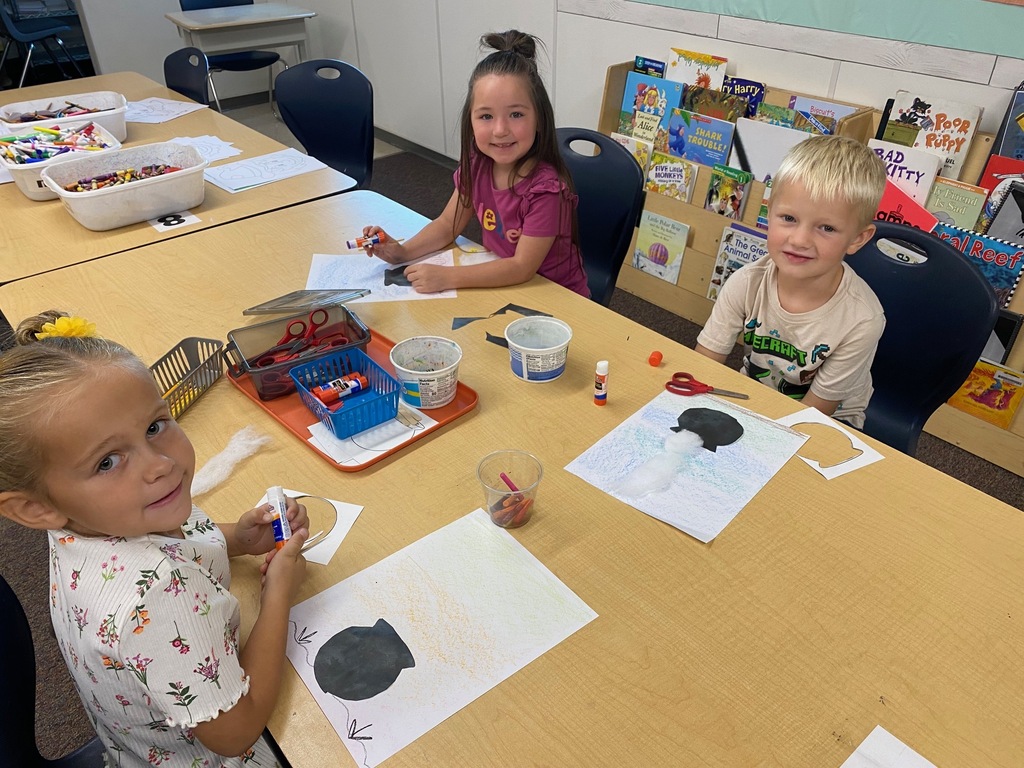 kindergarten students smiling with cauldron drawings, cutting, and actively creating art