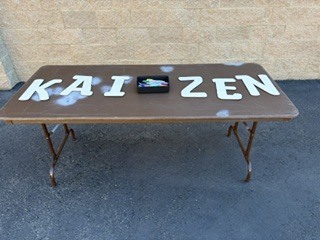 The letters KAIZEN with markers sitting on a brown table outside of the school