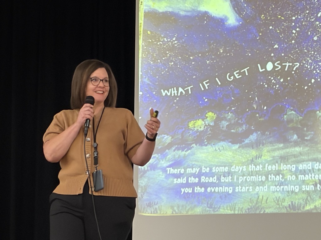 superintendent reading to students, standing in front of book portrayed on the screen